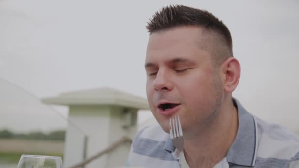 Een jongeman is lunchen met een salade met groenten in een restaurant op het open terras. Gezonde voeding. — Stockvideo