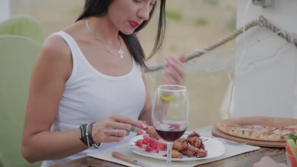 Una mujer disfruta comiendo alitas de pollo frito en un restaurante en la terraza abierta . — Vídeos de Stock