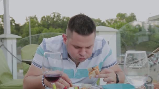 Un hombre come con entusiasmo comida chatarra en un restaurante . — Vídeo de stock