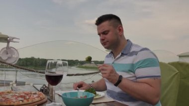 Genç bir adam açık terasta bir restoranda sebze li salata ile öğle yemeği yiyor. Sağlıklı gıda.