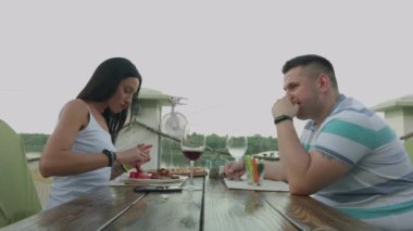 Açık terasta bir restoranda öğle yemeği alan genç erkek ve kadın.