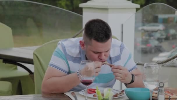 Un hombre come con entusiasmo comida chatarra en un restaurante . — Vídeo de stock