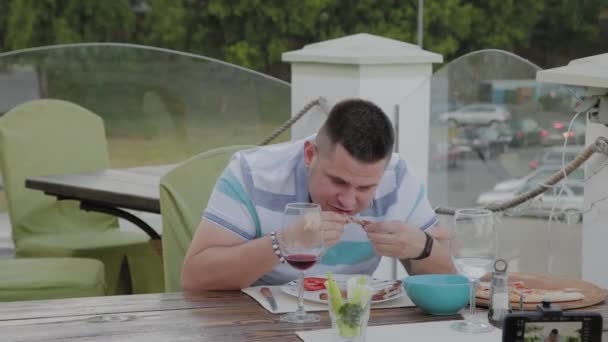 Un hombre come con entusiasmo comida chatarra en un restaurante . — Vídeos de Stock