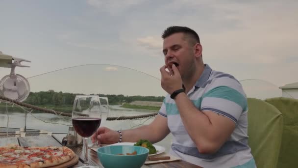 Um jovem está almoçando com uma salada com legumes em um restaurante no terraço aberto. Alimentos saudáveis . — Vídeo de Stock