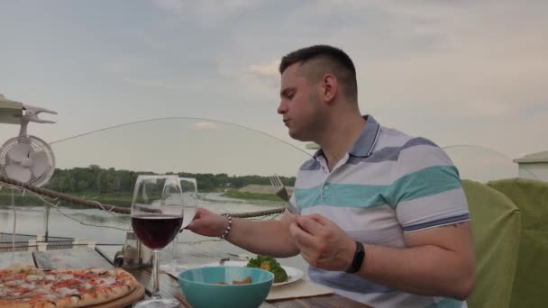 Ein junger Mann isst in einem Restaurant auf der offenen Terrasse zu Mittag mit Salat und Gemüse. gesunde Ernährung. — Stockvideo