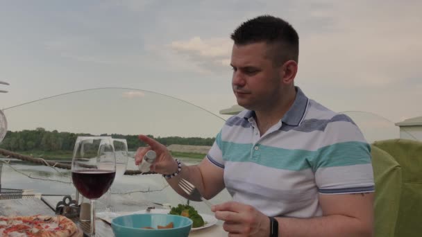 Ein junger Mann isst in einem Restaurant auf der offenen Terrasse zu Mittag mit Salat und Gemüse. gesunde Ernährung. — Stockvideo