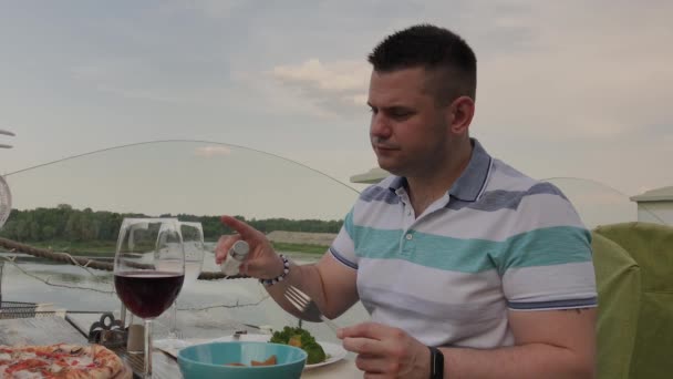 Un joven está almorzando con una ensalada con verduras en un restaurante en la terraza abierta. Alimento saludable . — Vídeos de Stock