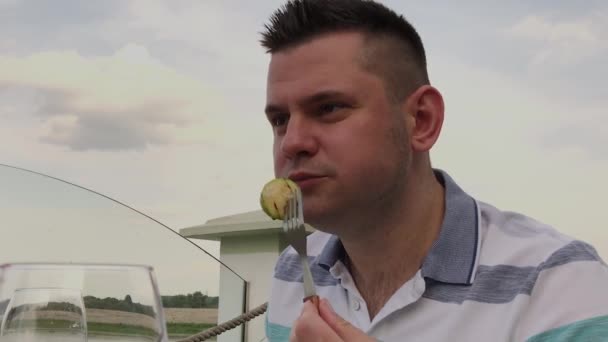 Een jongeman is lunchen met een salade met groenten in een restaurant op het open terras. Gezonde voeding. — Stockvideo