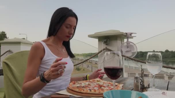 Schöne Frau isst Pizza auf der Terrasse eines Restaurants. — Stockvideo