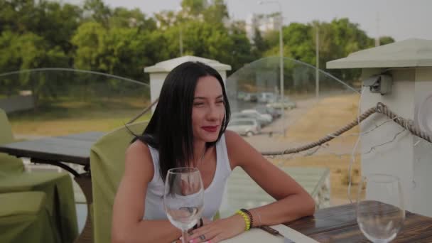 Красива жінка сидить за столом на терасі в ресторані . — стокове відео