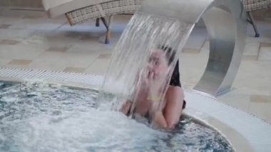 Güzel kız kapalı havuzda bir şelale altında yüzer.