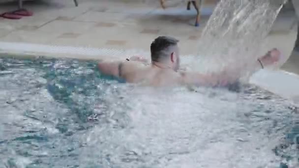 Hombre alegre nada bajo una cascada y posa en la piscina . — Vídeo de stock