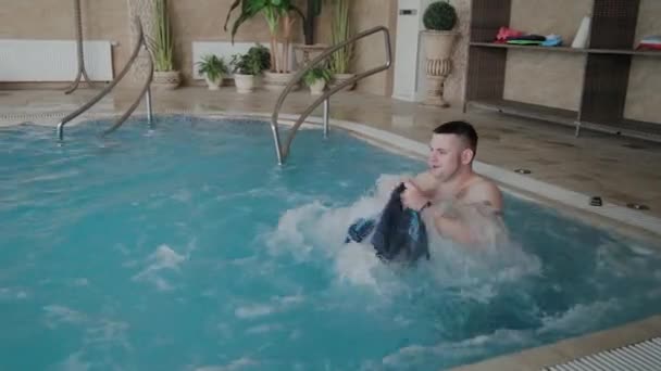 Alegre hombre divertido se baña en el jacuzzi de la piscina y lava sus pantalones cortos . — Vídeos de Stock
