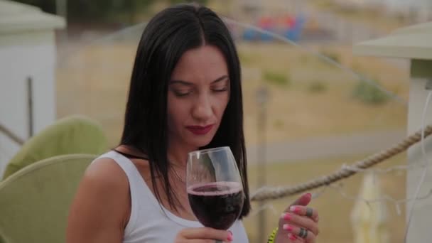 Gyönyörű nő iszik vörösbort a teraszon egy étteremben. — Stock videók