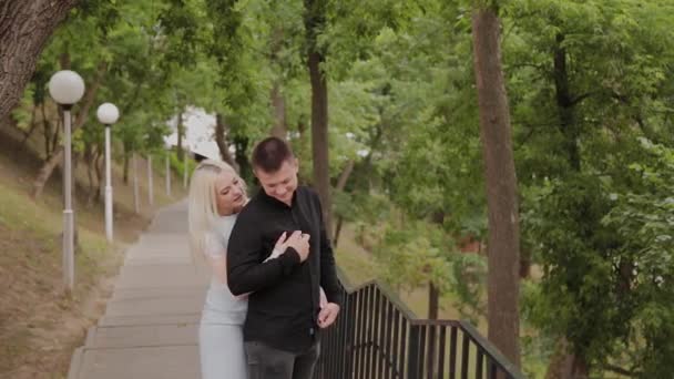 Pareja feliz enamorada se para en el descenso en el parque bajo los árboles . — Vídeo de stock