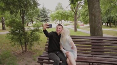 Mutlu çift aşk şehir parkında bir bankta oturan ve telefonda selfie yapma.