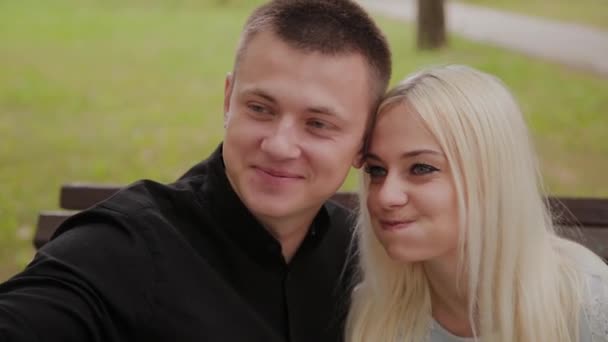 Happy couple in love sitting on a bench in the city park and making selfie on the phone. — Stock Video