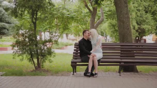 Pareja feliz enamorada sentada en un banco en un parque de la ciudad . — Vídeos de Stock