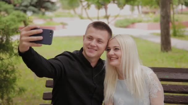 Mutlu çift aşk şehir parkında bir bankta oturan ve telefonda selfie yapma. — Stok video