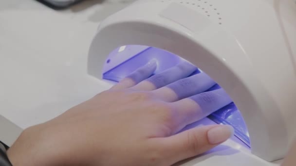 A young girl dries nail polish under an ultraviolet lamp in the manicure salon. — Stock Video