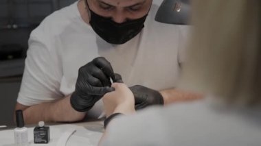 Profesyonel manikürcü adam vernishes bir kız çivi.