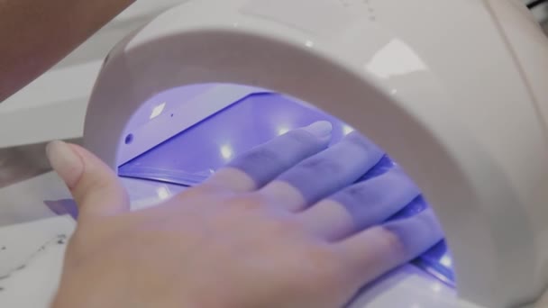 Een jong meisje droogt nagellak onder een ultraviolet lamp in de manicure salon. — Stockvideo