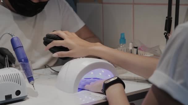 Ein junges Mädchen trocknet im Manikürsalon unter einer UV-Lampe Nagellack. — Stockvideo