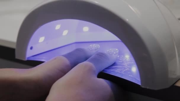Молодая девушка сушит лак для ногтей под ультрафиолетовой лампой в маникюрном салоне . — стоковое видео