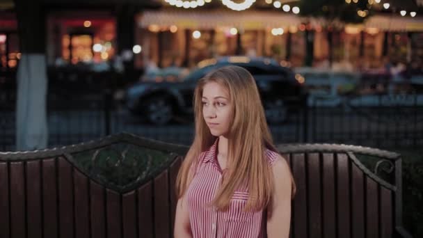 Hermosa joven en un banco por la noche en un parque . — Vídeo de stock