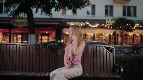 Beautiful young girl on a bench in the evening in a park. — Stock Video