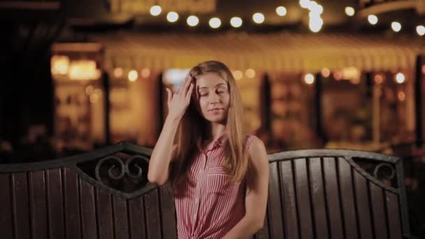 Beautiful young girl on a bench in the evening in a park. — Stock Video