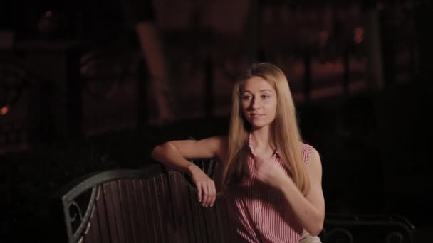 Menina bonita em um banco à noite em um parque . — Vídeo de Stock