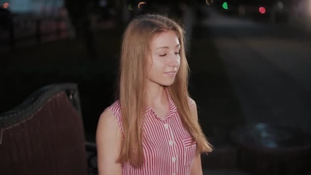 Bella ragazza su una panchina la sera in un parco . — Video Stock