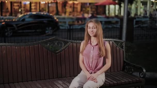 美丽的年轻女孩在长椅上在公园的晚上. — 图库视频影像
