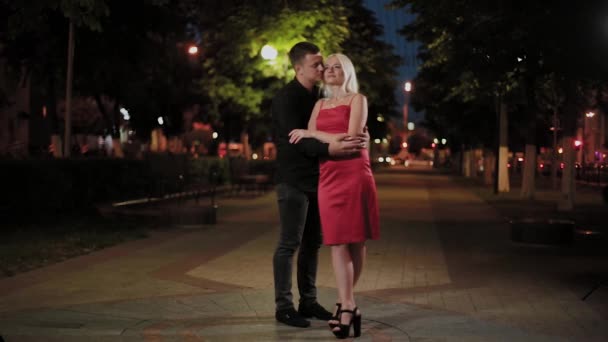 Счастливые влюбленные обнимаются на городской аллее вечером в свете фонарей . — стоковое видео