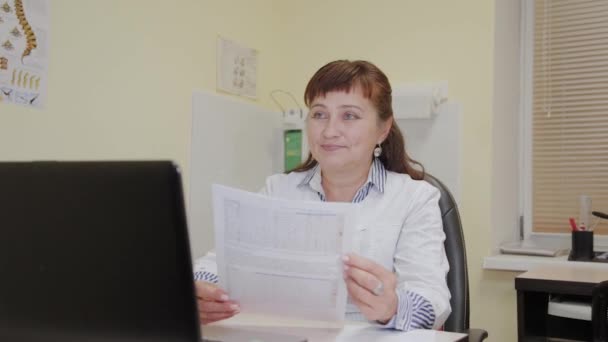 En äldre kvinna läkare tar ett testresultat från en skrivare och undersöker det. — Stockvideo
