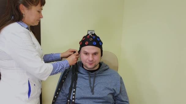 El médico le pone a un hombre un auricular para el estudio del cerebro humano . — Vídeos de Stock