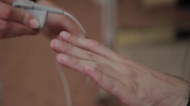 Klinikteki bir hastaya, erkek hemşire vücut parametrelerini incelemek için vücuduna bir cihaz koyar..