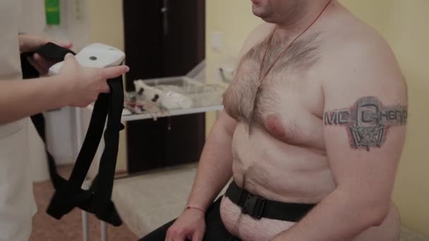 Klinikteki bir hastaya, erkek hemşire vücut parametrelerini incelemek için vücuduna bir cihaz koyar.. — Stok video