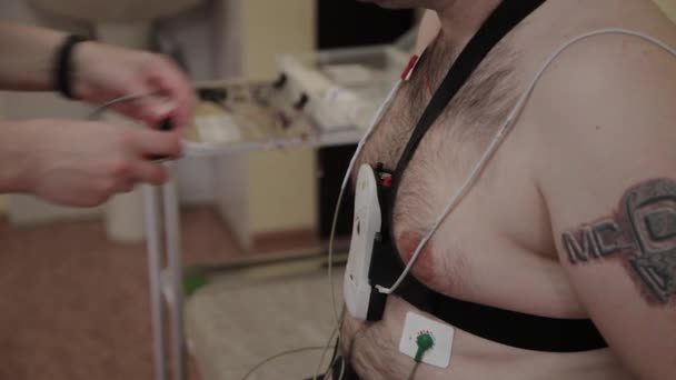 To a patient in a clinic, a male nurse puts a device on his body to study body parameters. — Stock Video