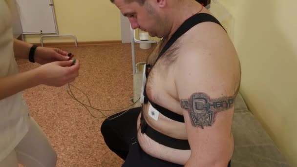 Klinikteki bir hastaya, erkek hemşire vücut parametrelerini incelemek için vücuduna bir cihaz koyar.. — Stok video