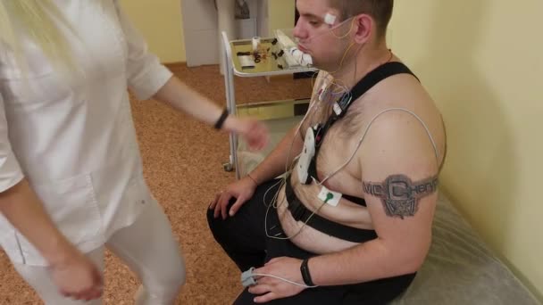 Till en patient på en klinik, en manlig sjuksköterska sätter en enhet på hans kropp att studera kroppsparametrar. — Stockvideo