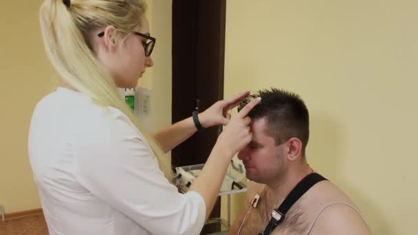 Aan een patiënt in een kliniek zet een mannelijke verpleegkundige een apparaat op zijn lichaam om lichaamsparameters te bestuderen. — Stockvideo