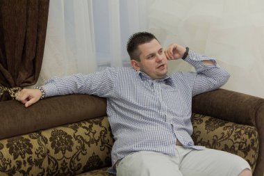 Genç adam bir düğün salonunda bir kanepeye oturur.