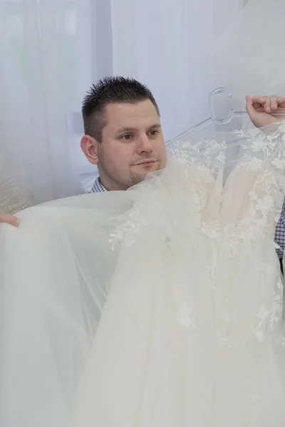 Homme tient des robes de mariée dans un salon de mariée . — Photo