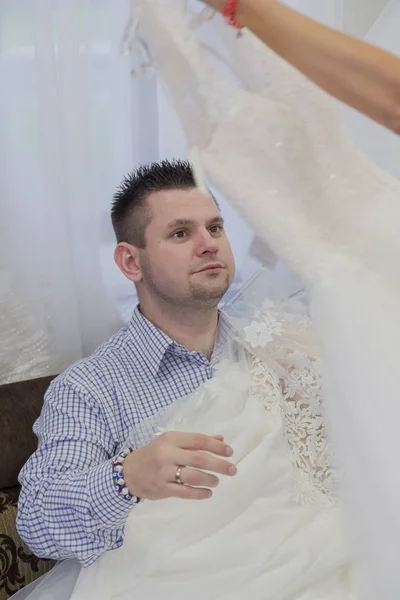 Homem mantém vestidos de noiva em um salão de noivas . — Fotografia de Stock