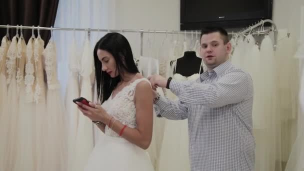 Knappe man vastmaakt een trouwjurk aan zijn vrouw in een bruiloft salon. — Stockvideo