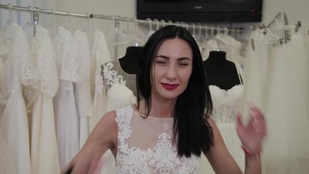 Hermosa chica mide un vestido de novia en un salón de novias . — Vídeos de Stock