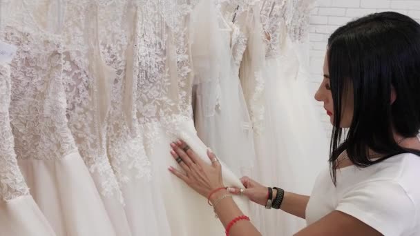 Hermosa chica elige un vestido de novia en un salón de novia . — Vídeo de stock