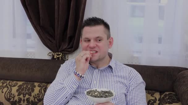 Knappe man eet zwarte zaden op een bank. — Stockvideo